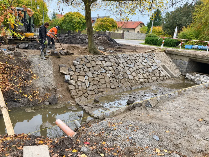 Pracovníci při úpravě břehu s kamenným opevněním vedle mostku
