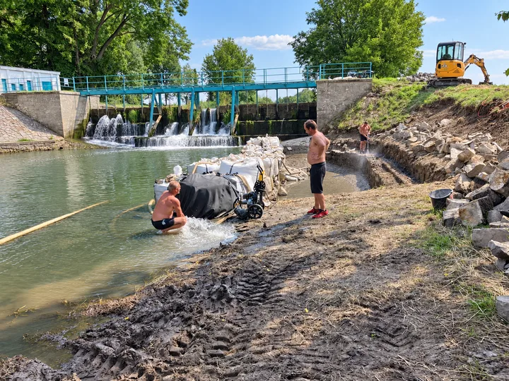 Pracovníci, čerpací technika a bagr při pracích na břehu u jezu