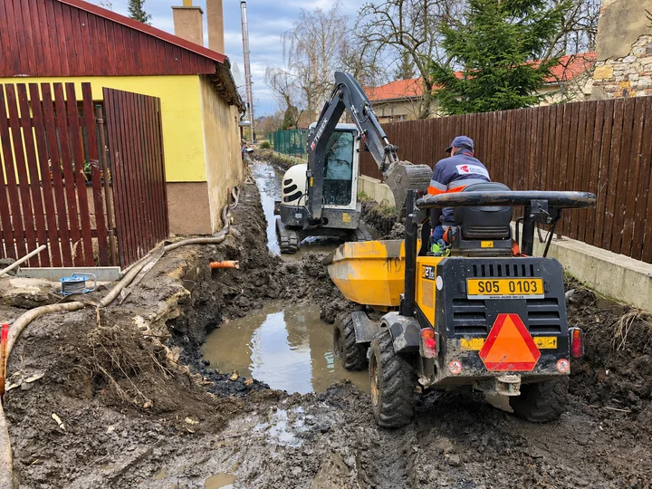 Minibagr a žlutý dumper ve výkopu v úzkém průjezdu mezi domem a plotem