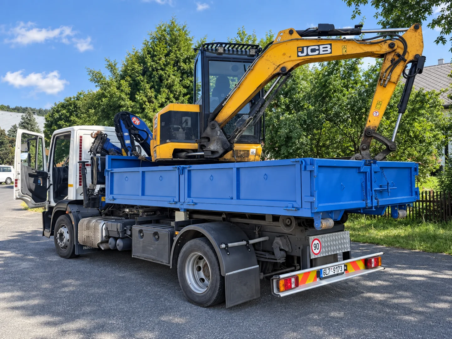 Náš bagr JCB na modrém nákladním voze Iveco s hydraulickou rukou